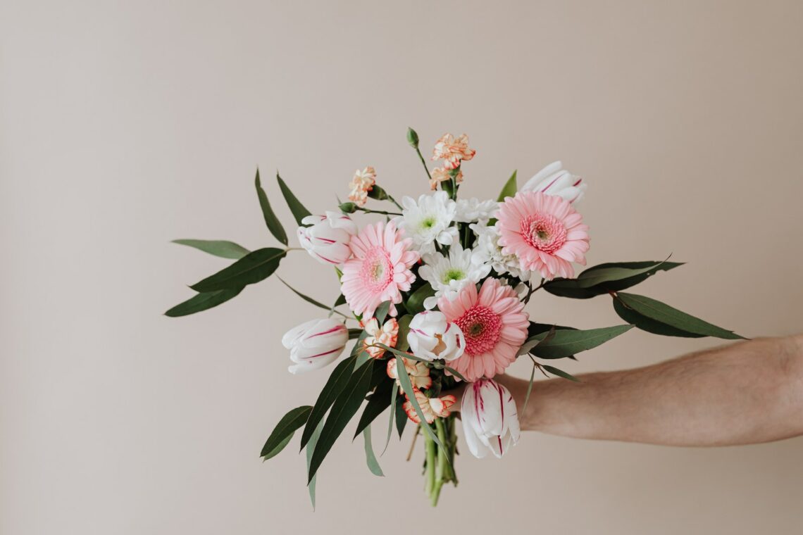 Unrecognizable male holding bunch of fresh chamomiles cloves and gerberas during making tender spring composition against beige background