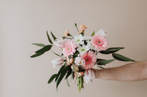 Unrecognizable male holding bunch of fresh chamomiles cloves and gerberas during making tender spring composition against beige background