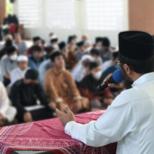 a person in a white shirt and black hat speaking into a microphone