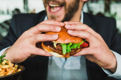 person holding burger bun with vegetables and meat