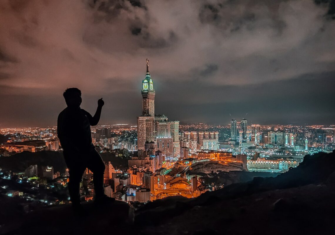 man in black jacket standing on rock near body of water during night time