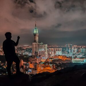 man in black jacket standing on rock near body of water during night time