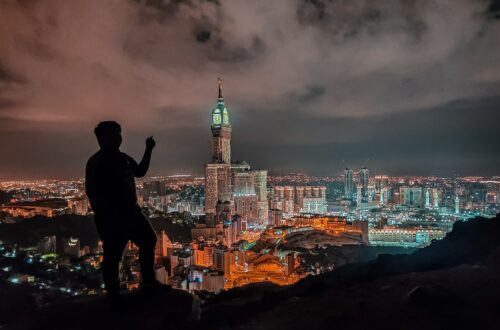 man in black jacket standing on rock near body of water during night time