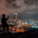 man in black jacket standing on rock near body of water during night time